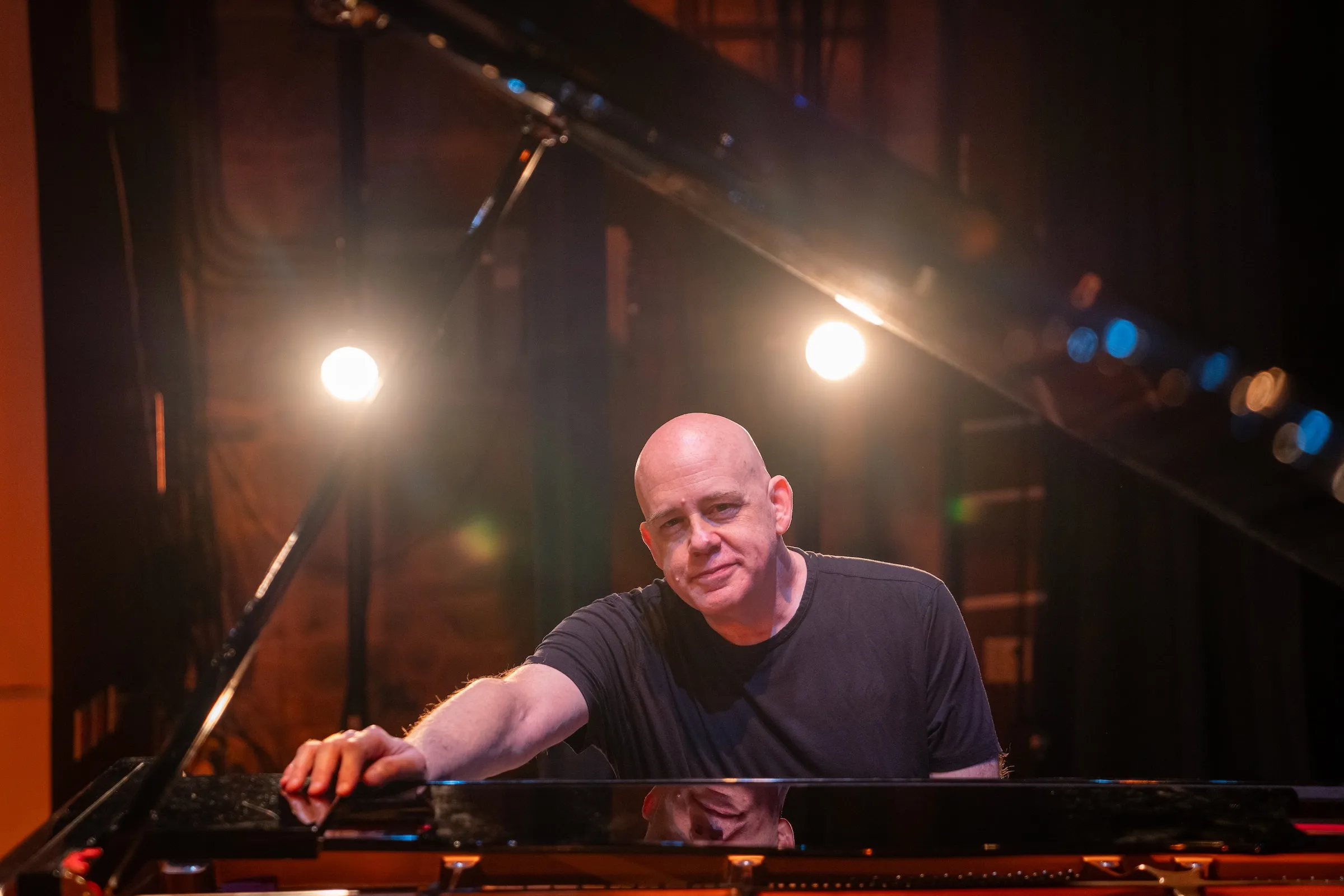 Brian Shaw leaning on an open grand piano on a lit stage.